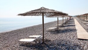 Una playa de guijarros con sillones de madera y sombrillas de paja.