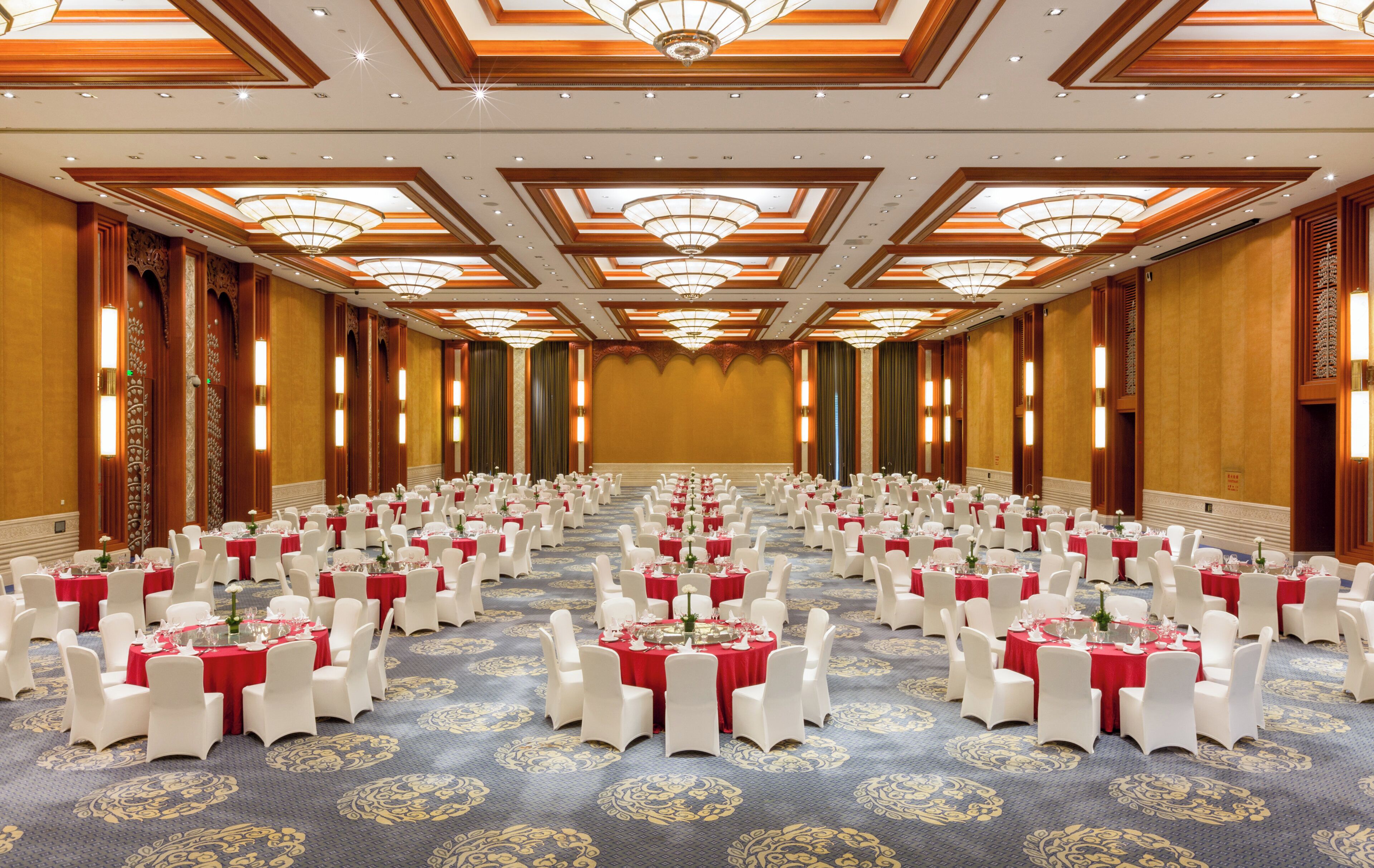 A large banquet hall with rows of round tables, each with white chairs and red tablecloths.