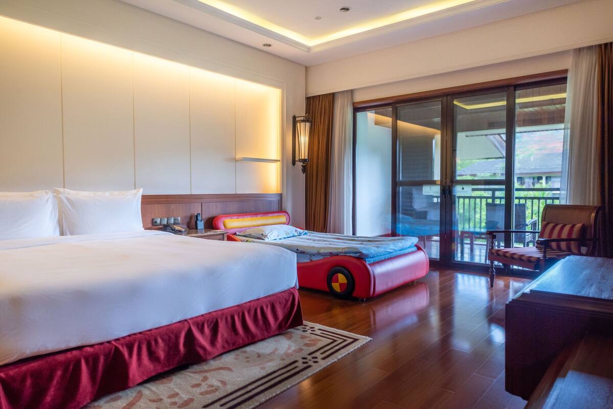 A hotel room with a large bed, a smaller bed, a sofa, and a balcony with a view.