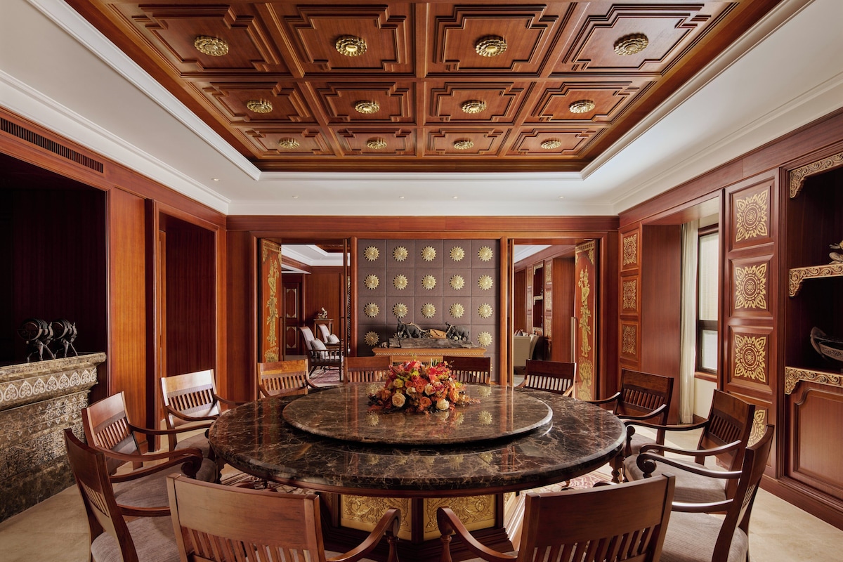 A formal dining room with a round marble table, wooden chairs, and a decorative ceiling.