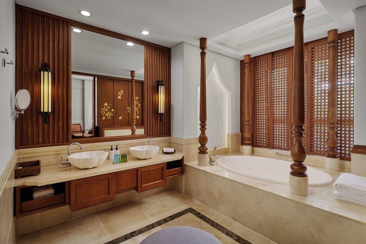 A spacious bathroom with a large mirror, two sinks, a bathtub, wooden paneling, and a decorative screen.