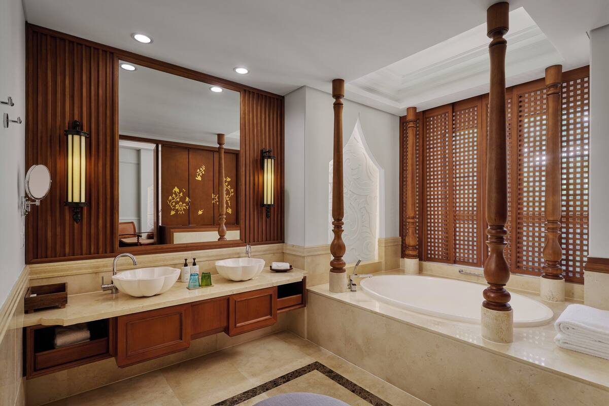 A spacious bathroom with a large mirror, two sinks, a bathtub, wooden paneling, and a decorative screen.