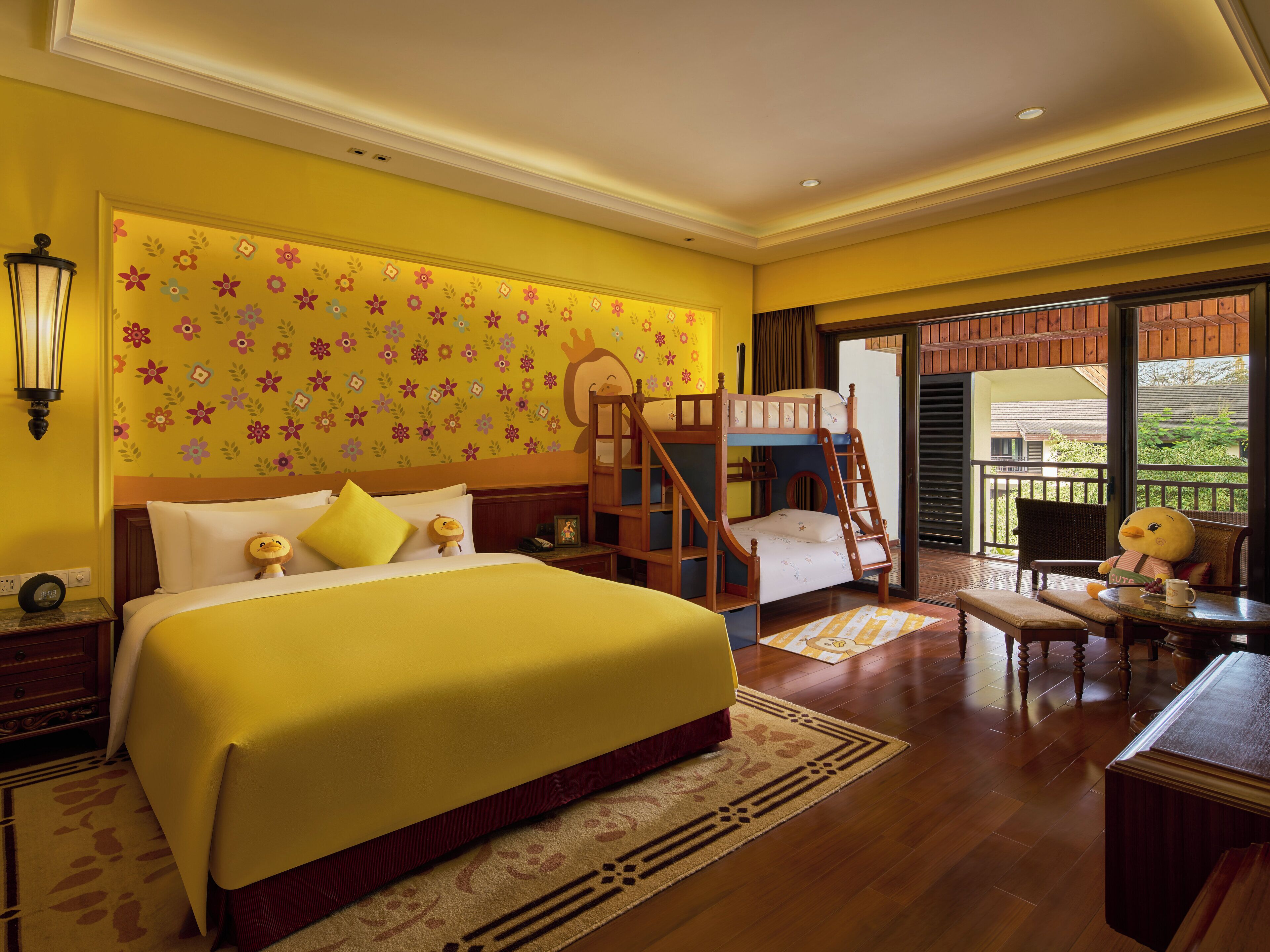 A hotel room with a large bed, a wooden bunk bed, a desk with a chair, and a balcony with a view.