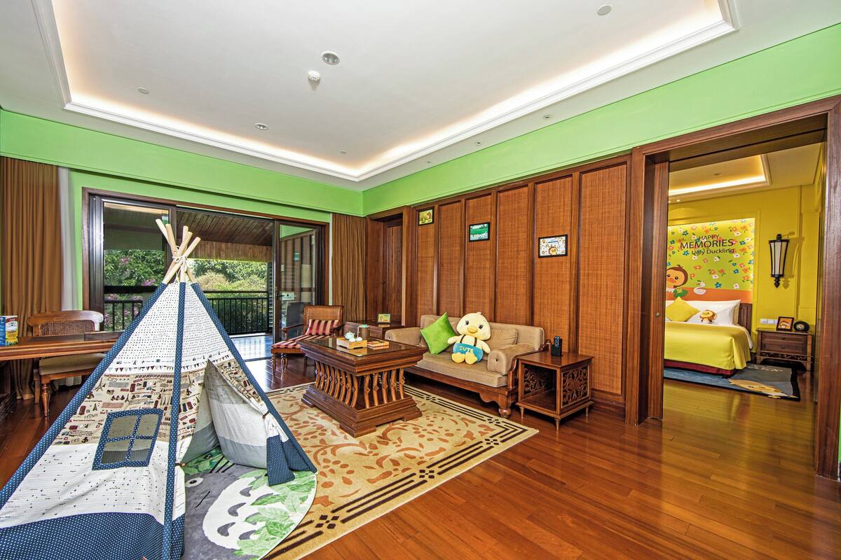 A cozy living room with a wooden floor, a sofa with a teddy bear, a coffee table, and a tent-like play area.