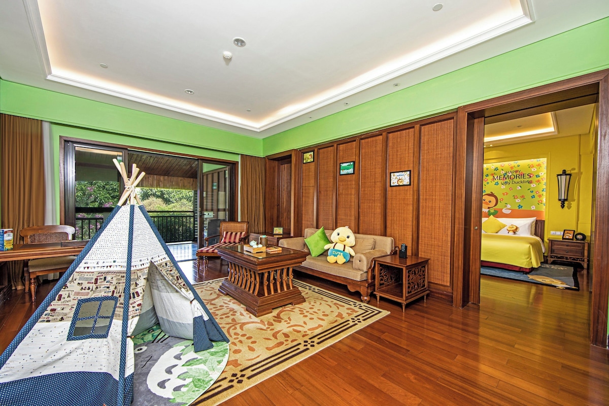 A cozy living room with a wooden floor, a sofa with a teddy bear, a coffee table, and a tent-like play area.
