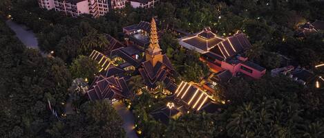 Vista aérea de un complejo turístico con varias edificaciones, incluyendo una estructura central con aguja, rodeado de exuberante vegetación y palmeras.