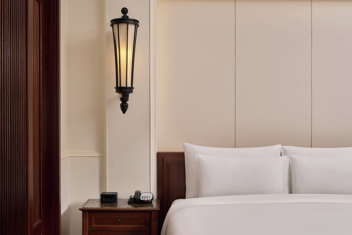 A hotel room with a bed, a nightstand with a lamp, and a telephone.