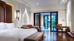 Amplia habitación de hotel con una cama grande, zona de estar con sofá y sillones, una mesa de comedor y vistas al exterior a través de un ventanal.