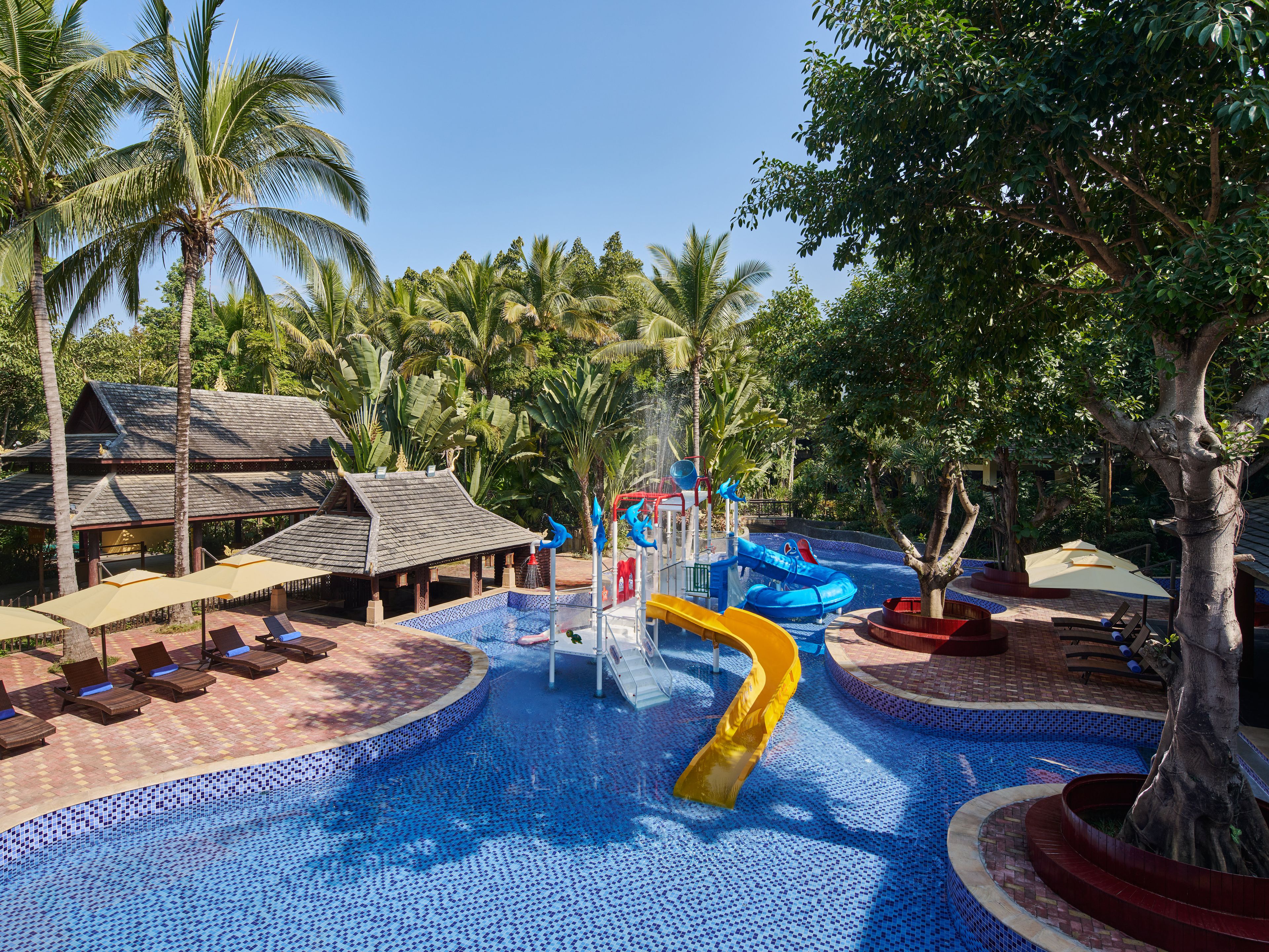 A pool area with a water slide, lounge chairs, and a covered seating area.