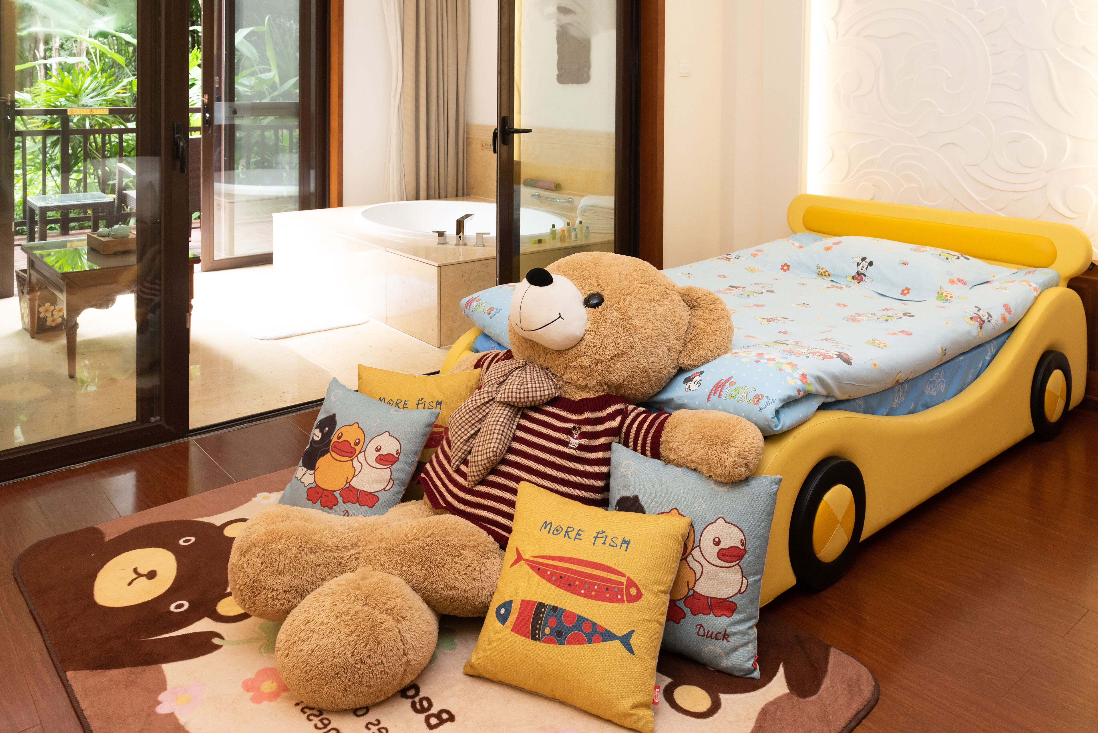 A child's bedroom with a bed, a teddy bear, and various pillows.