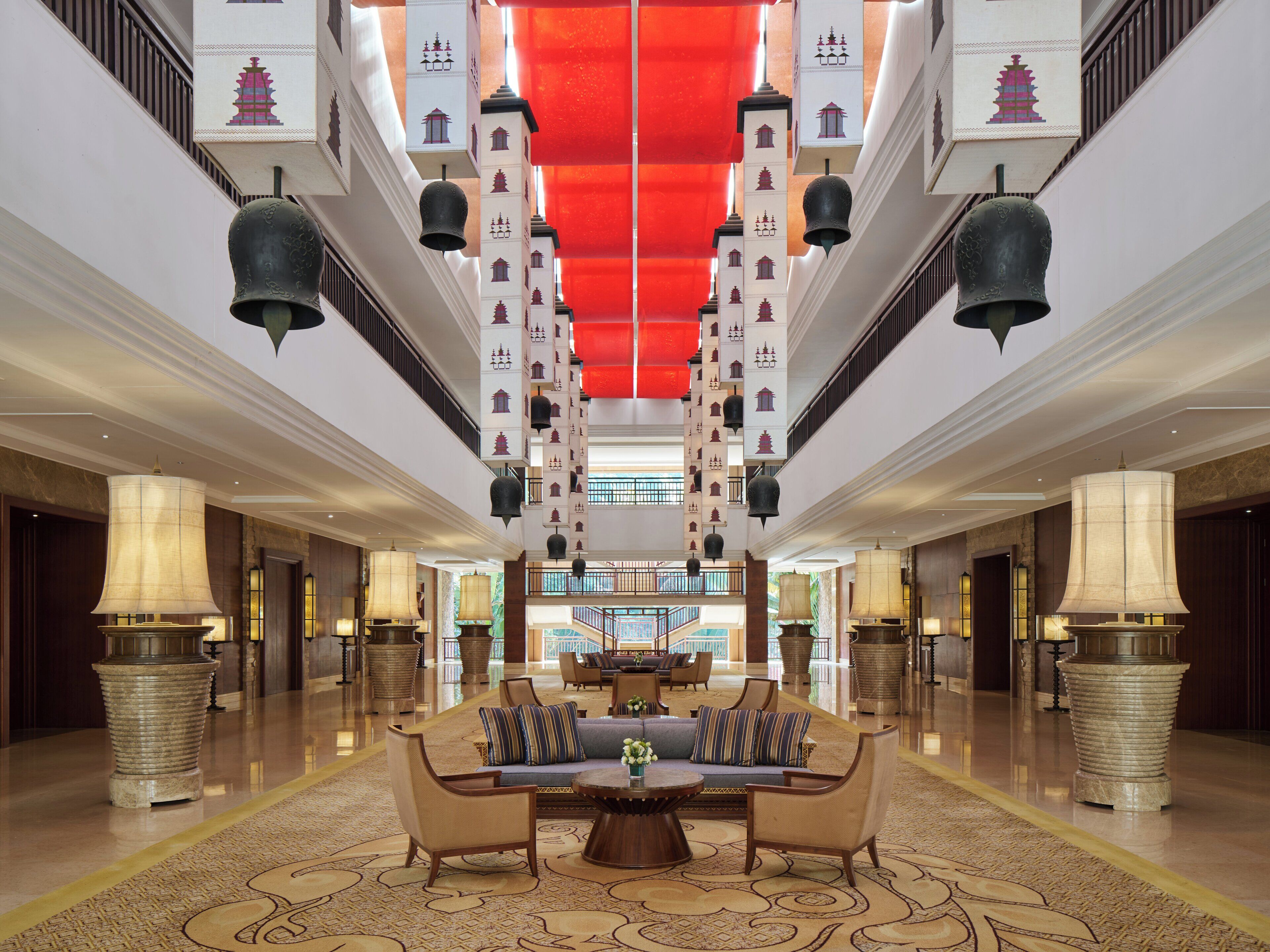 Een ruime lobby met een centraal zitgedeelte, een hoog plafond met decoratieve details, en een modern design.