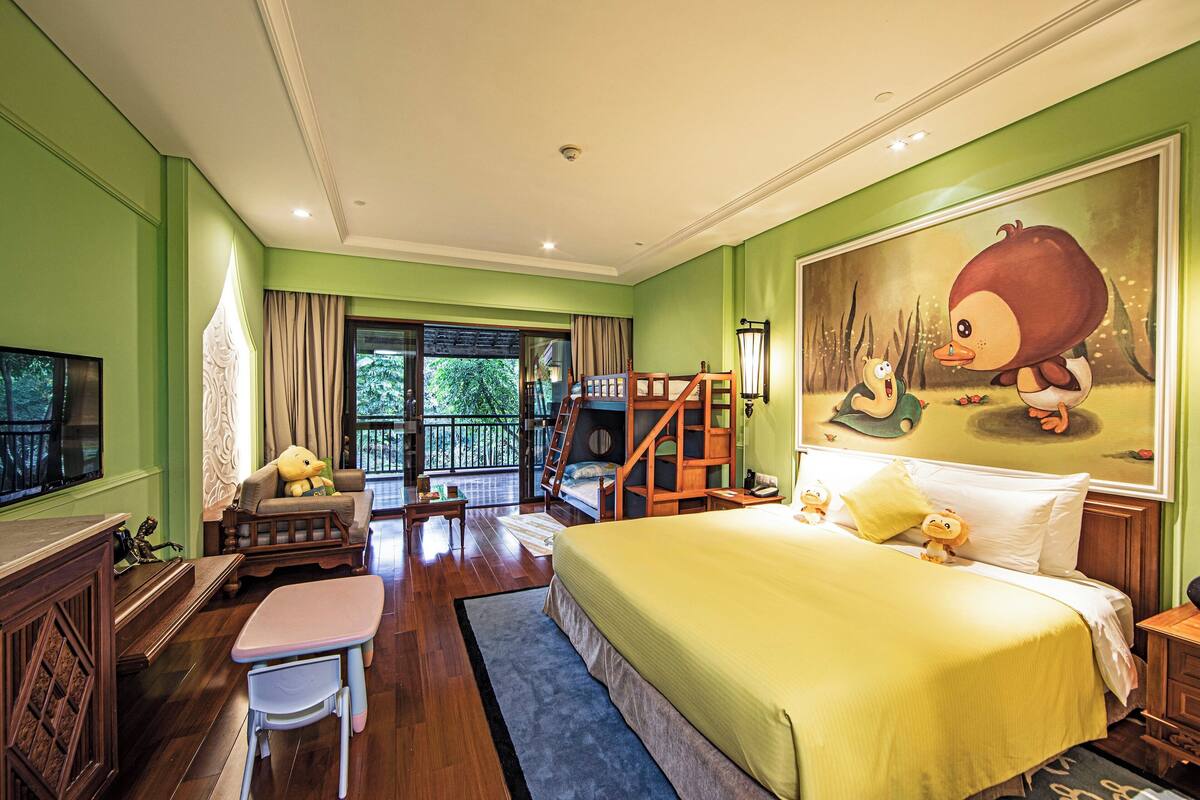A bedroom with a bunk bed, a large bed with pillows, a desk, and a chair.