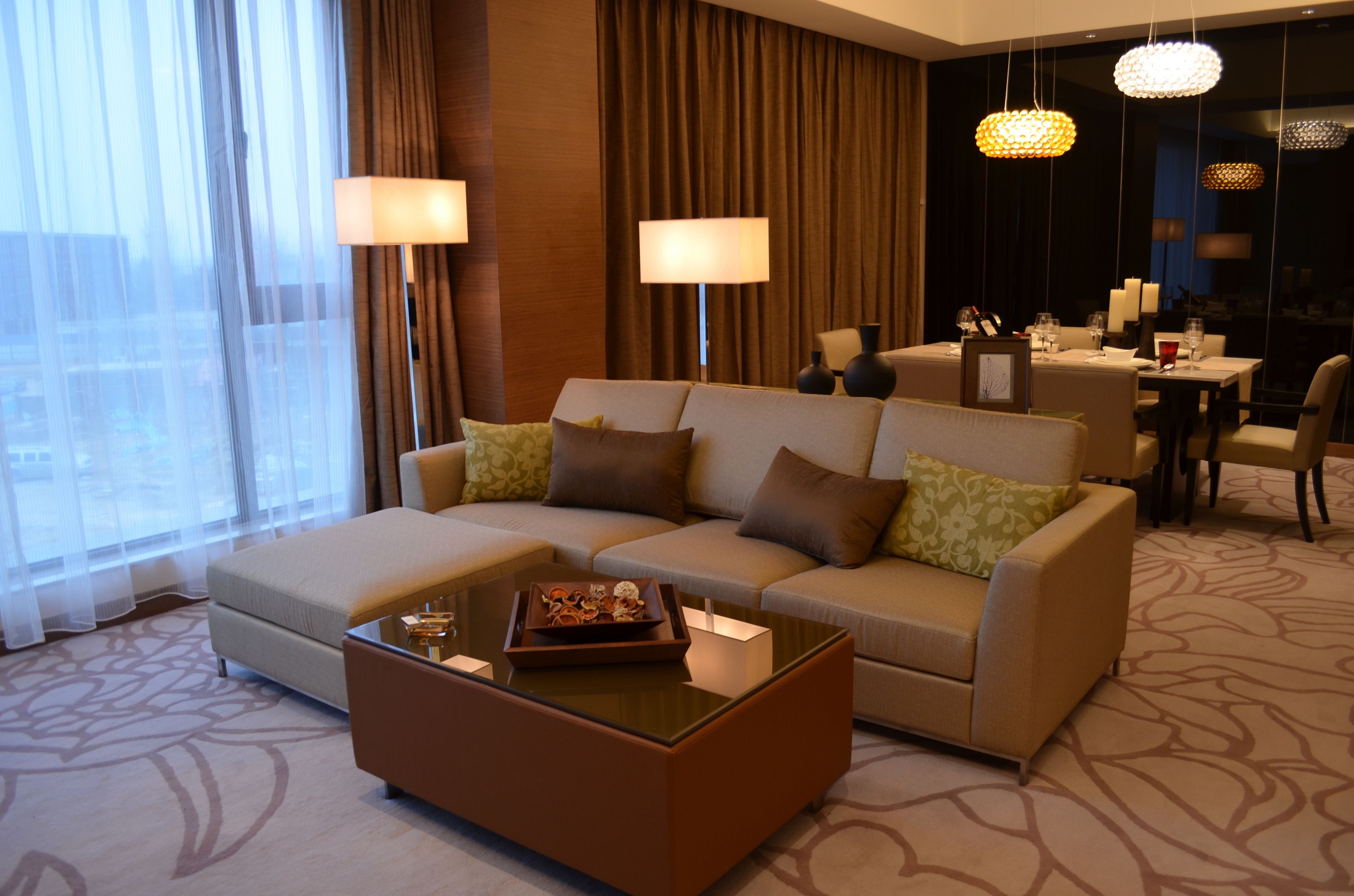 A modern hotel room with a sofa, a coffee table, and a dining area with a table and chairs.