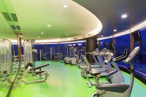 Ein Fitnessstudio mit unterschiedlichen Trainingsgeräten, darunter Laufbändern und Kraftmaschinen, und einem grünen Boden.