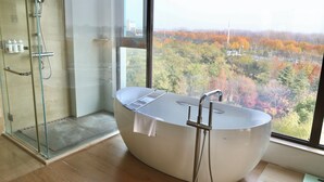 Une salle de bain moderne avec une baignoire sur pieds, une douche en verre et une vue sur le feuillage automnal grâce à de grandes fenêtres.