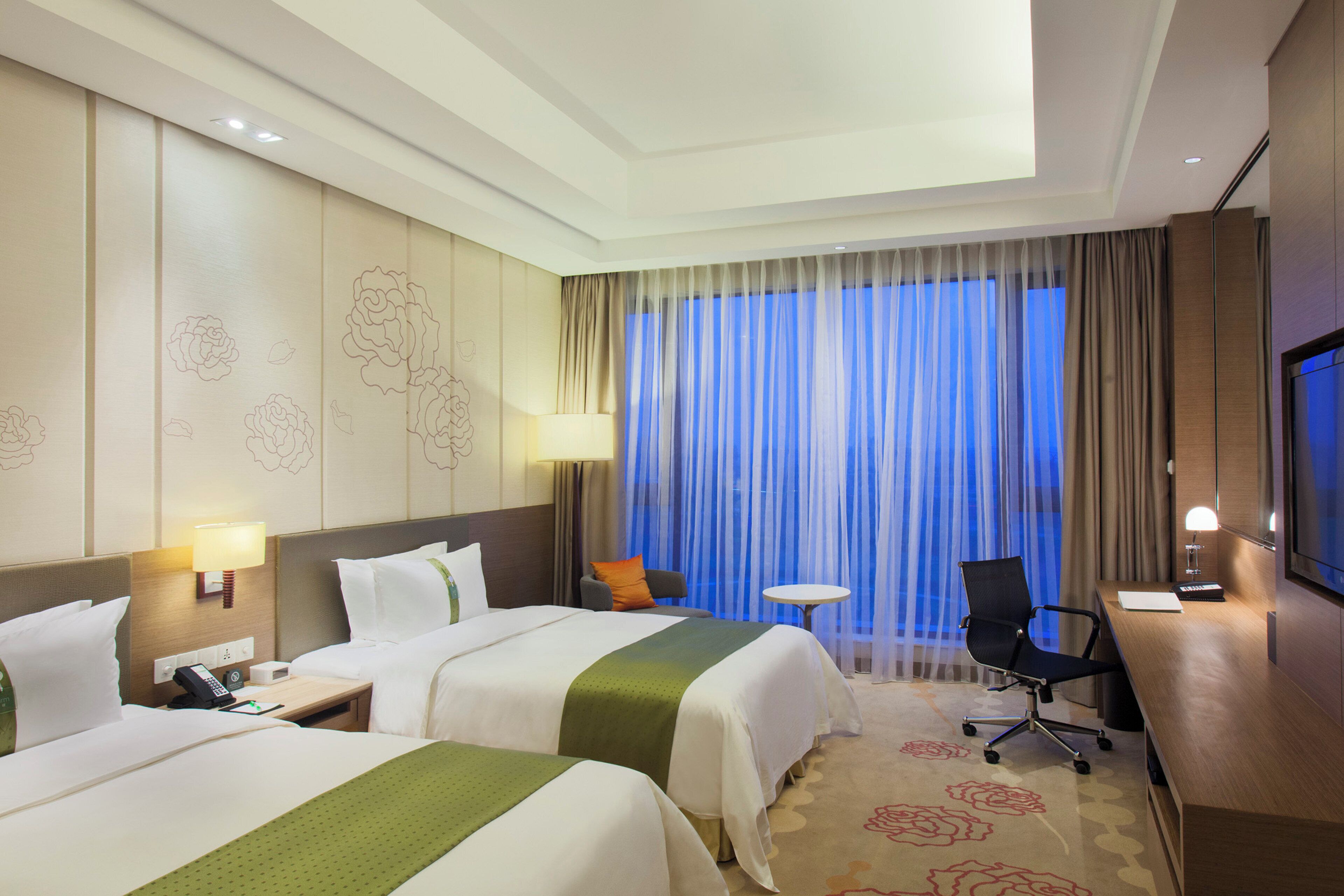Habitación de hotel con dos camas, un escritorio, una silla, un televisor y una ventana con cortinas.