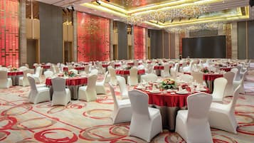 Un salón de banquetes con mesas redondas, sillas blancas y manteles rojos.