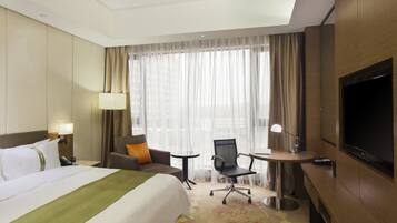 Una habitación de hotel con una cama grande, un escritorio con silla, televisión y ventana con cortinas.