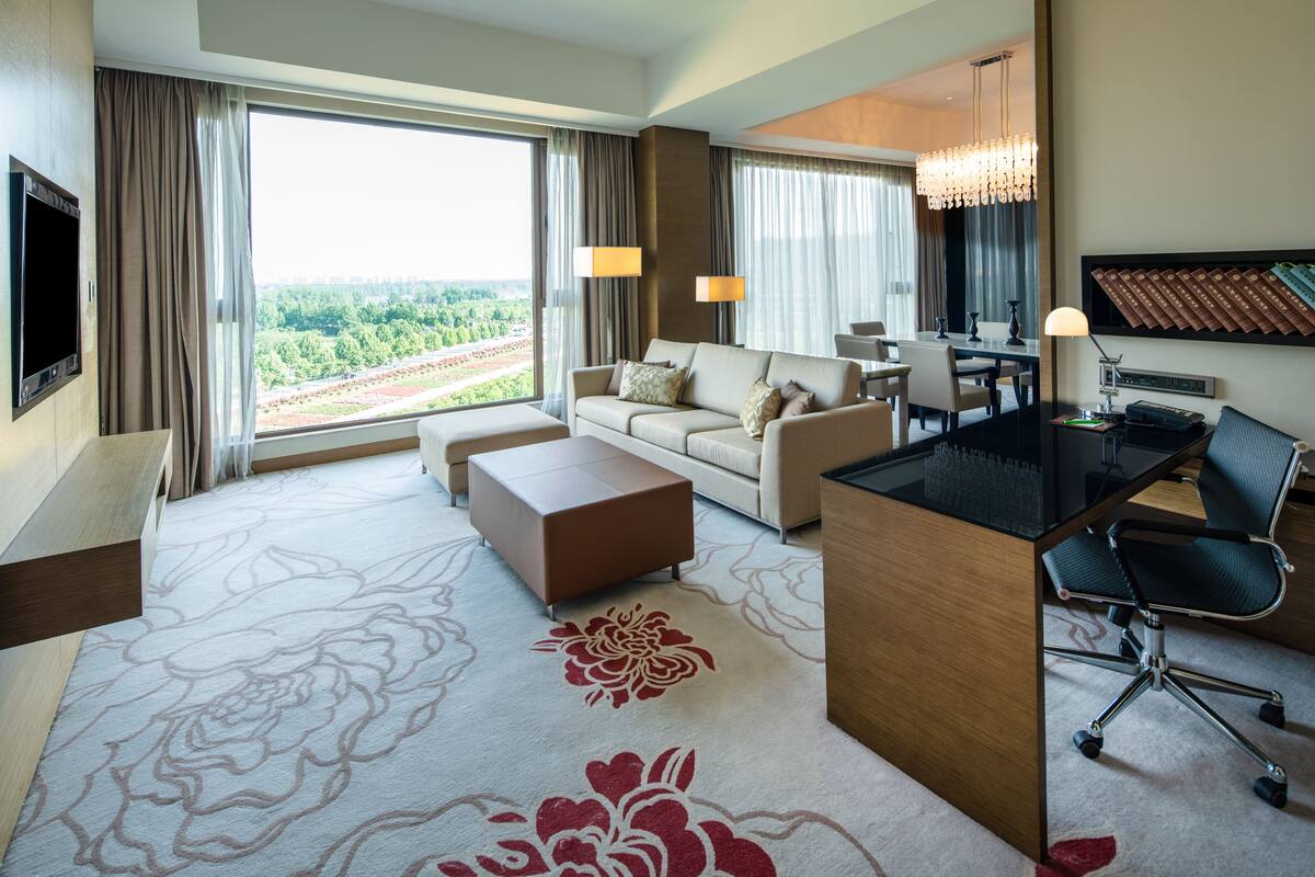 A hotel room with a large window, a sofa, a desk, and a chair.