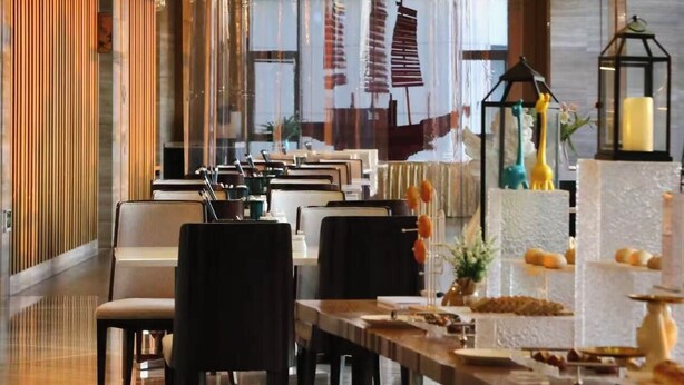 Un hall d’hôtel moderne avec un long comptoir d’accueil, des sièges confortables et un grand lustre.