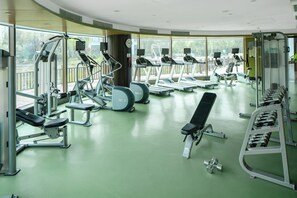 Ett gym med olika typer av träningsutrustning, stora fönster och ett grönt golv.