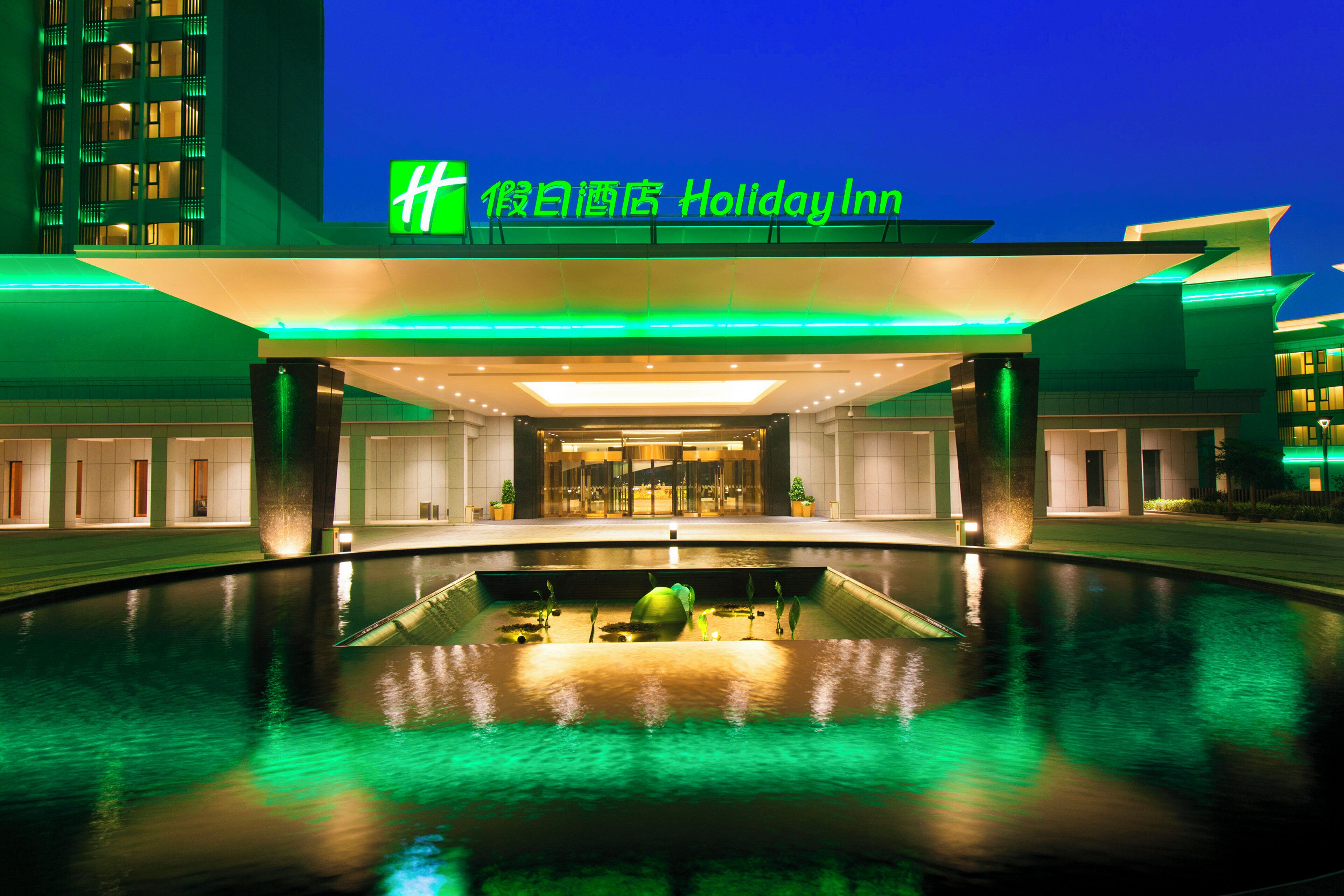 Un hotel con una entrada moderna, una piscina y un cartel que indica que es un Holiday Inn.