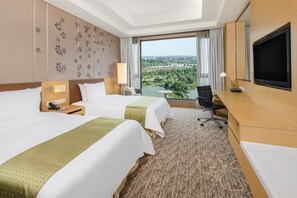 Quarto de hotel com duas camas, uma escrivaninha, uma televisão e vista para o horizonte urbano.