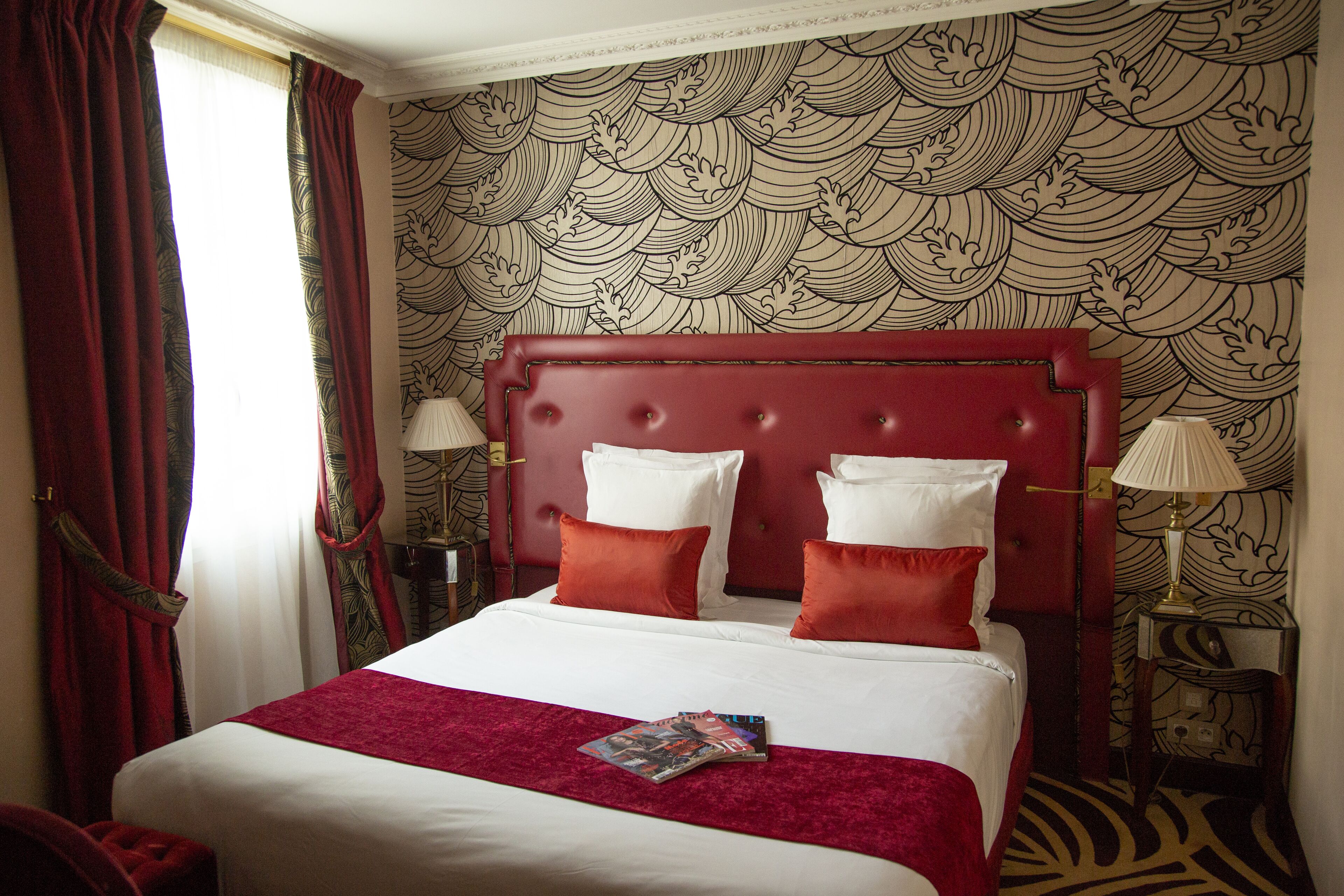 A hotel room with a large bed, red curtains, and a patterned wallpaper.