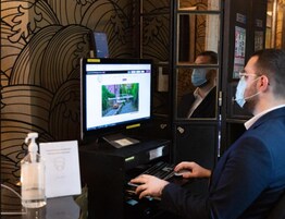A man using a laptop at a self-service kiosk with a monitor displaying a webpage.