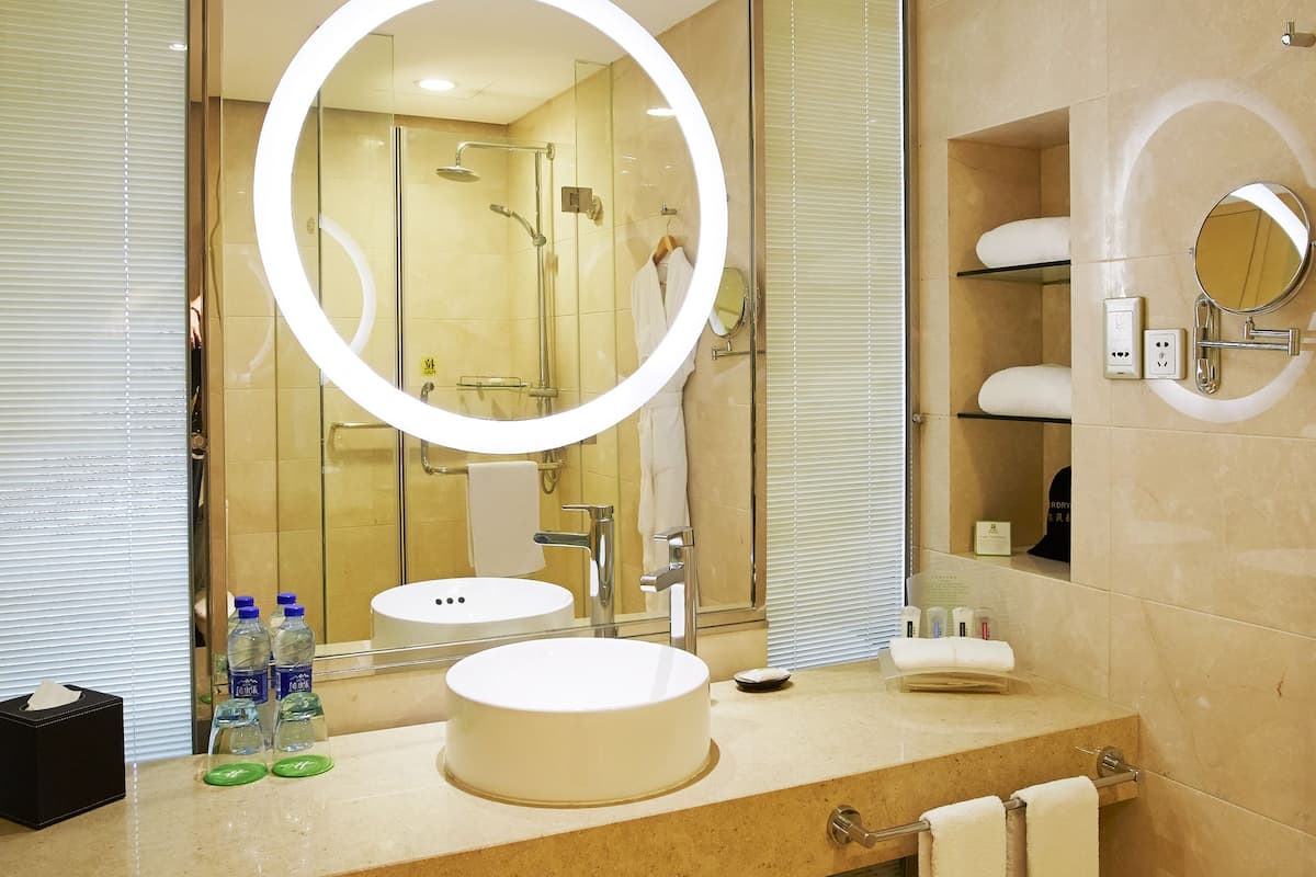 A modern bathroom with two sinks, a large mirror with a circular light, and a shower area.