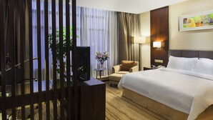 Ett hotellrum med en säng, en stol, ett skrivbord med en dator, en lampa och en tavla på väggen.