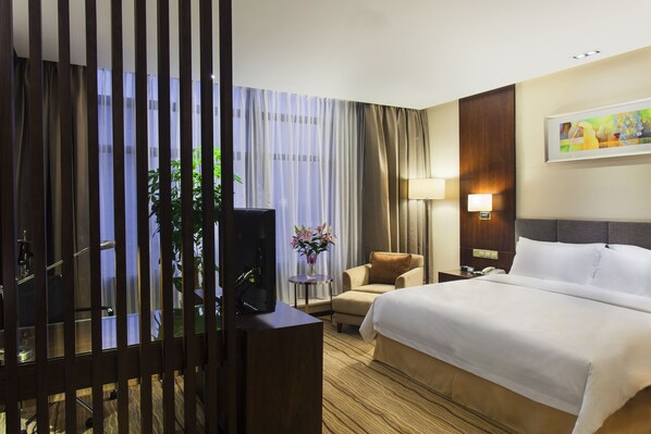 Une chambre d’hôtel avec un lit, une chaise, un bureau avec un ordinateur, une lampe et un tableau au mur.