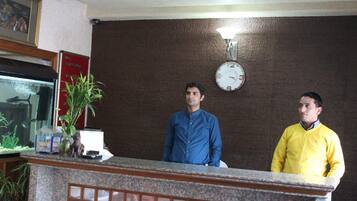 Un área de recepción con un reloj en la pared, un mostrador de recepción y una planta.