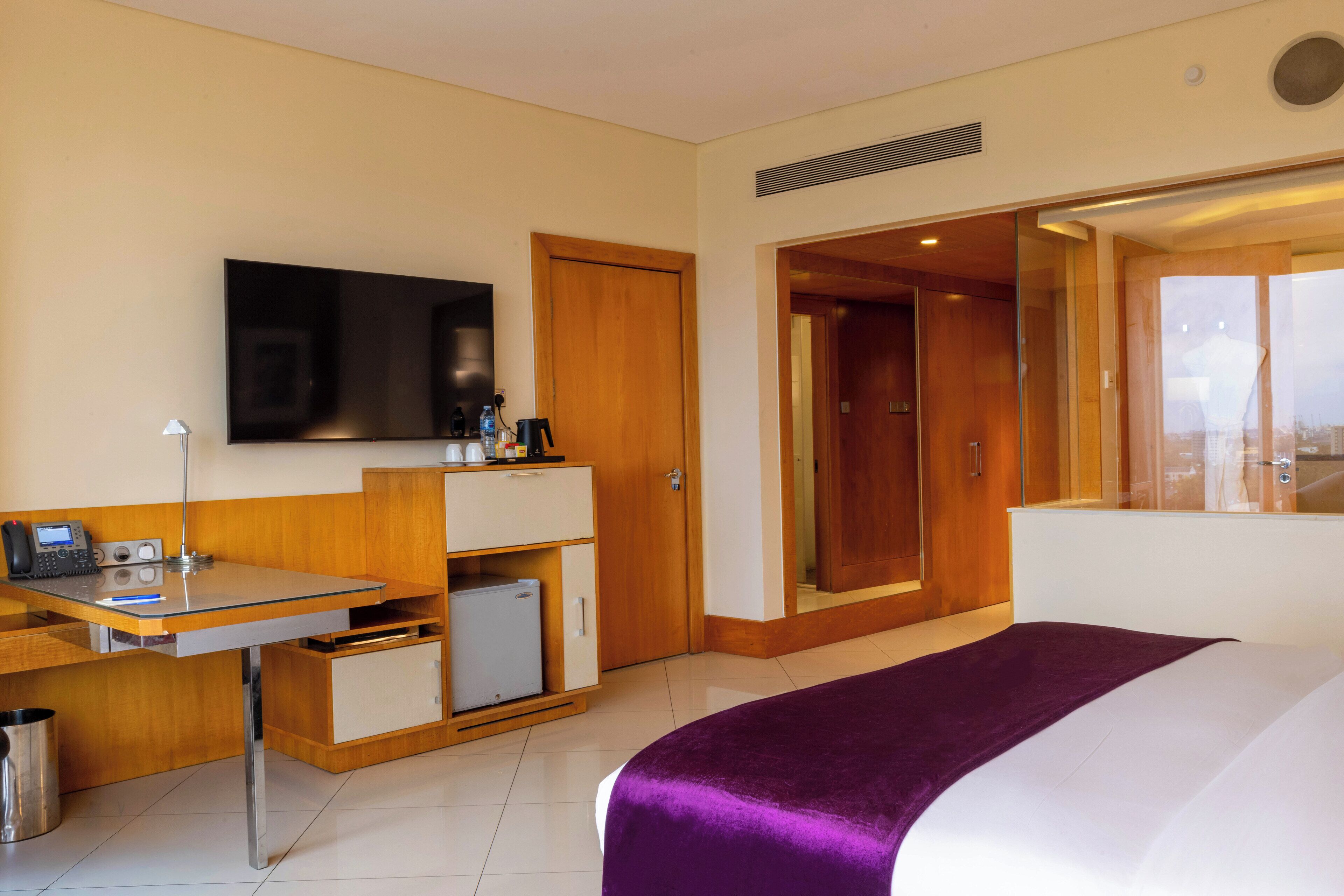 A hotel room with a bed, a desk with a computer, a television, and a minibar.