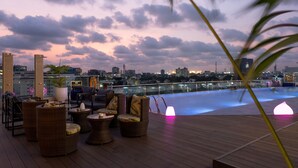 A rooftop lounge with wicker furniture, a pool, and a cityscape view at dusk. - Lagos Continental Hotel (Lagos)