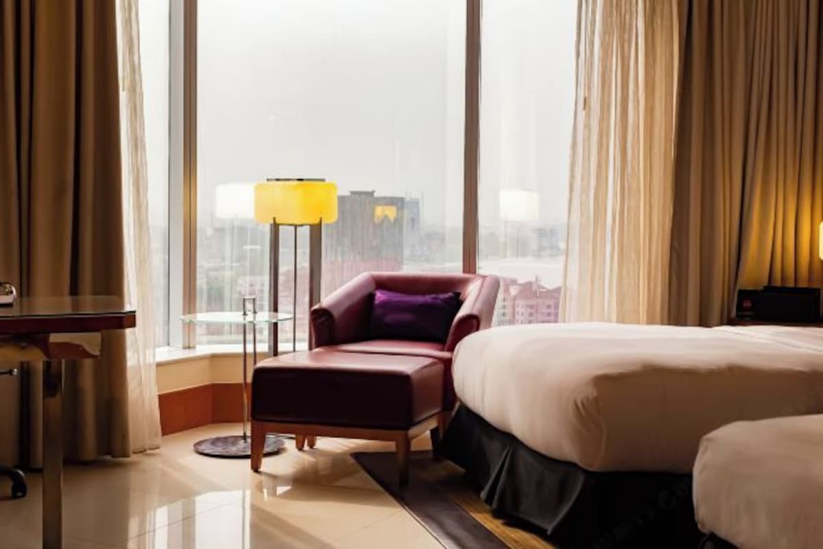 Quarto de hotel com uma cama grande, uma poltrona vermelha, uma mesinha e um abajur.