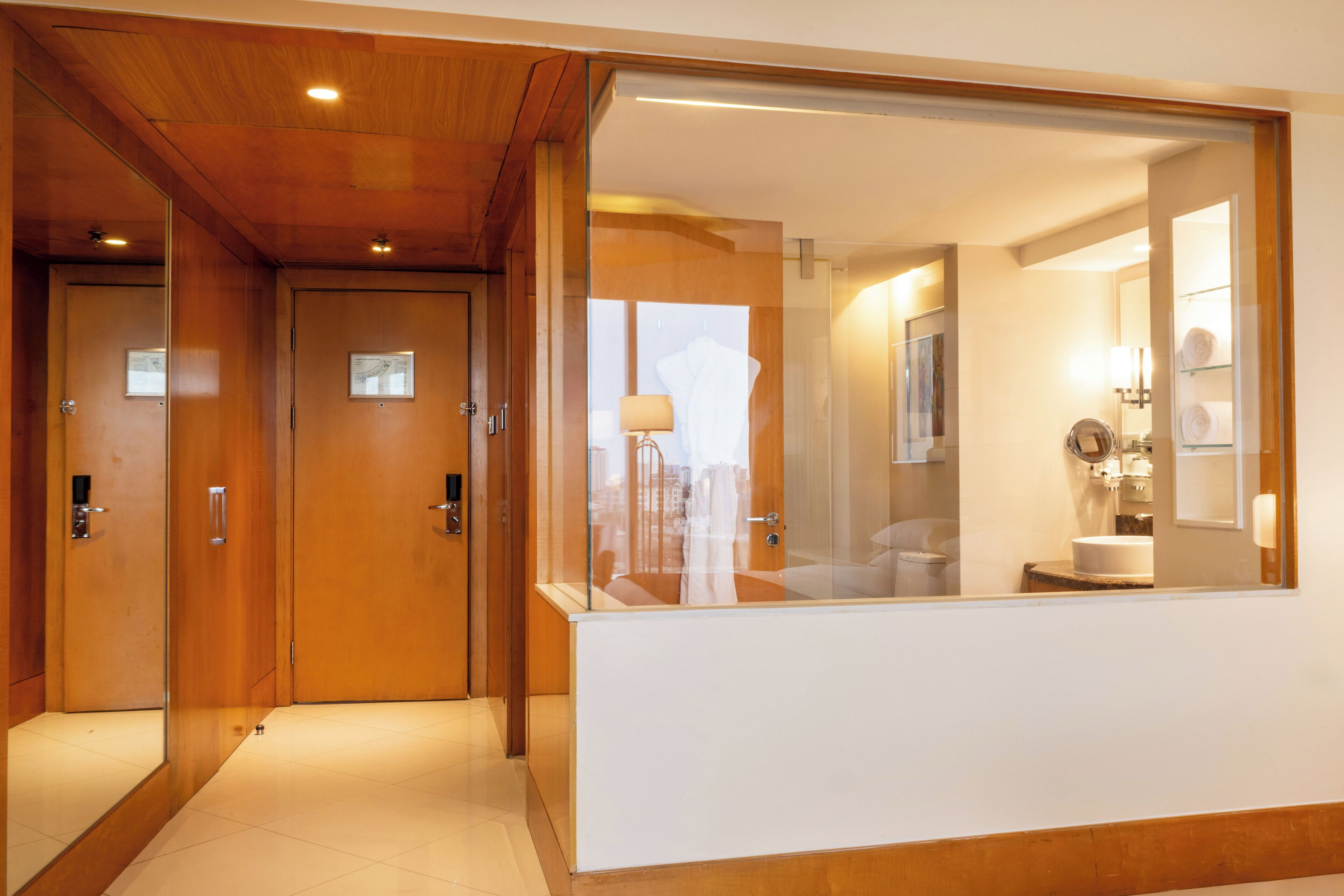 A hotel hallway with wooden doors, a reception desk, and a bathroom visible through a glass partition.
