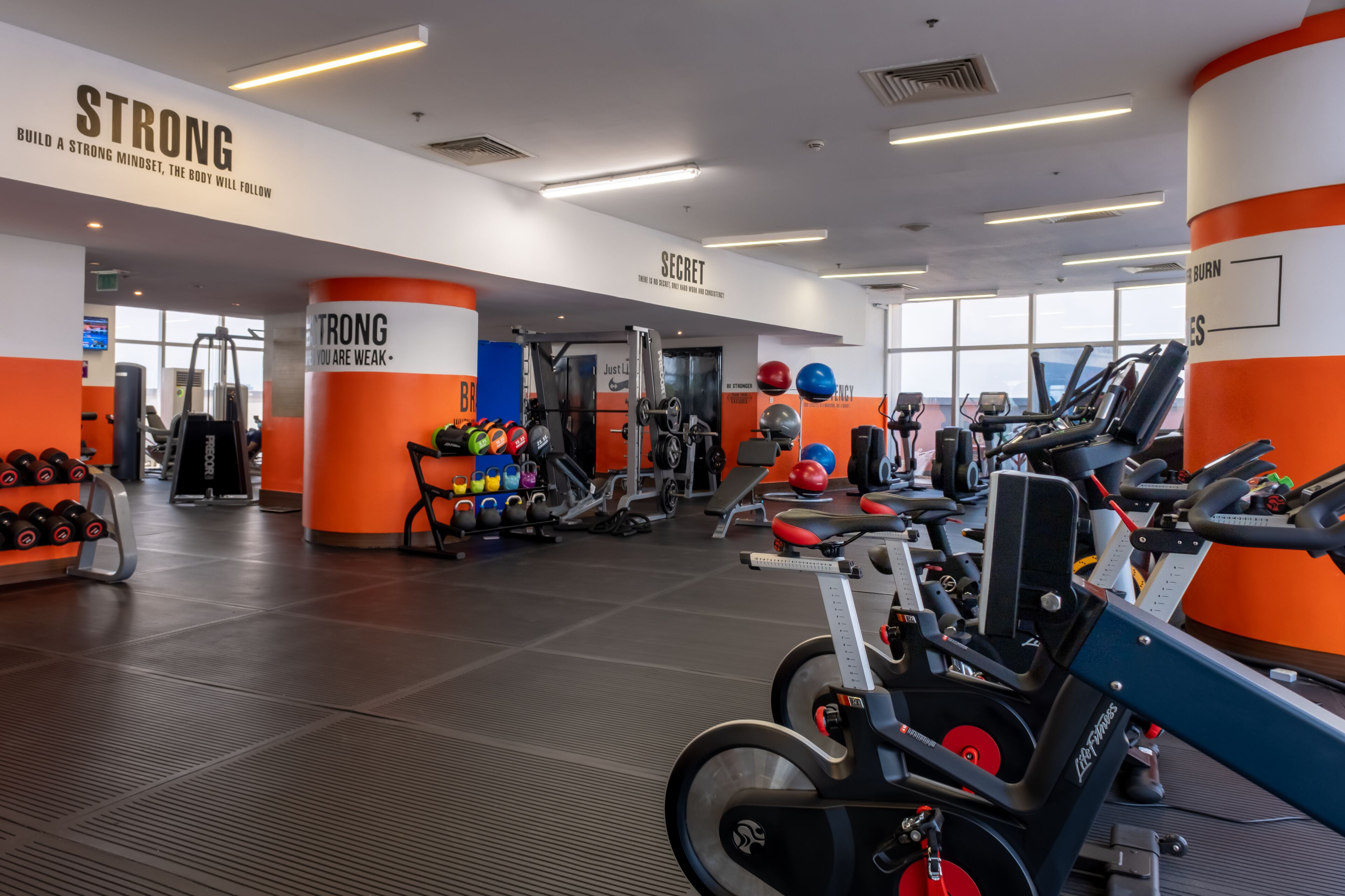 Un gimnasio con paredes anaranjadas y blancas, equipo de levantamiento de pesas y máquinas de ejercicio.
