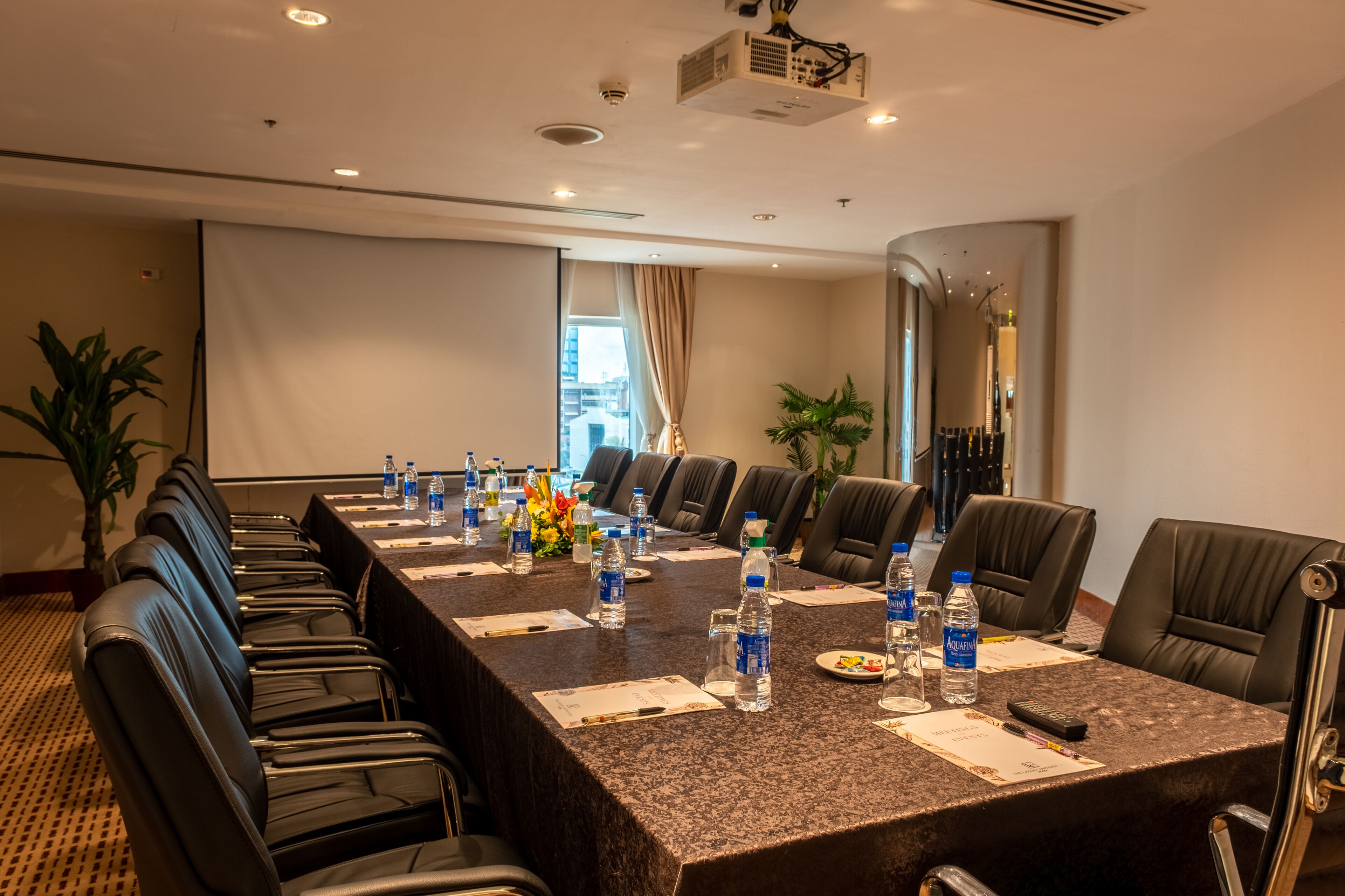 A conference room with a long table, black leather chairs, water bottles, and a projector.