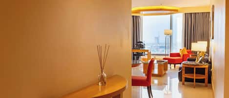 A hotel room with a wooden console table, a red chair, a sofa, a coffee table, and a lamp.