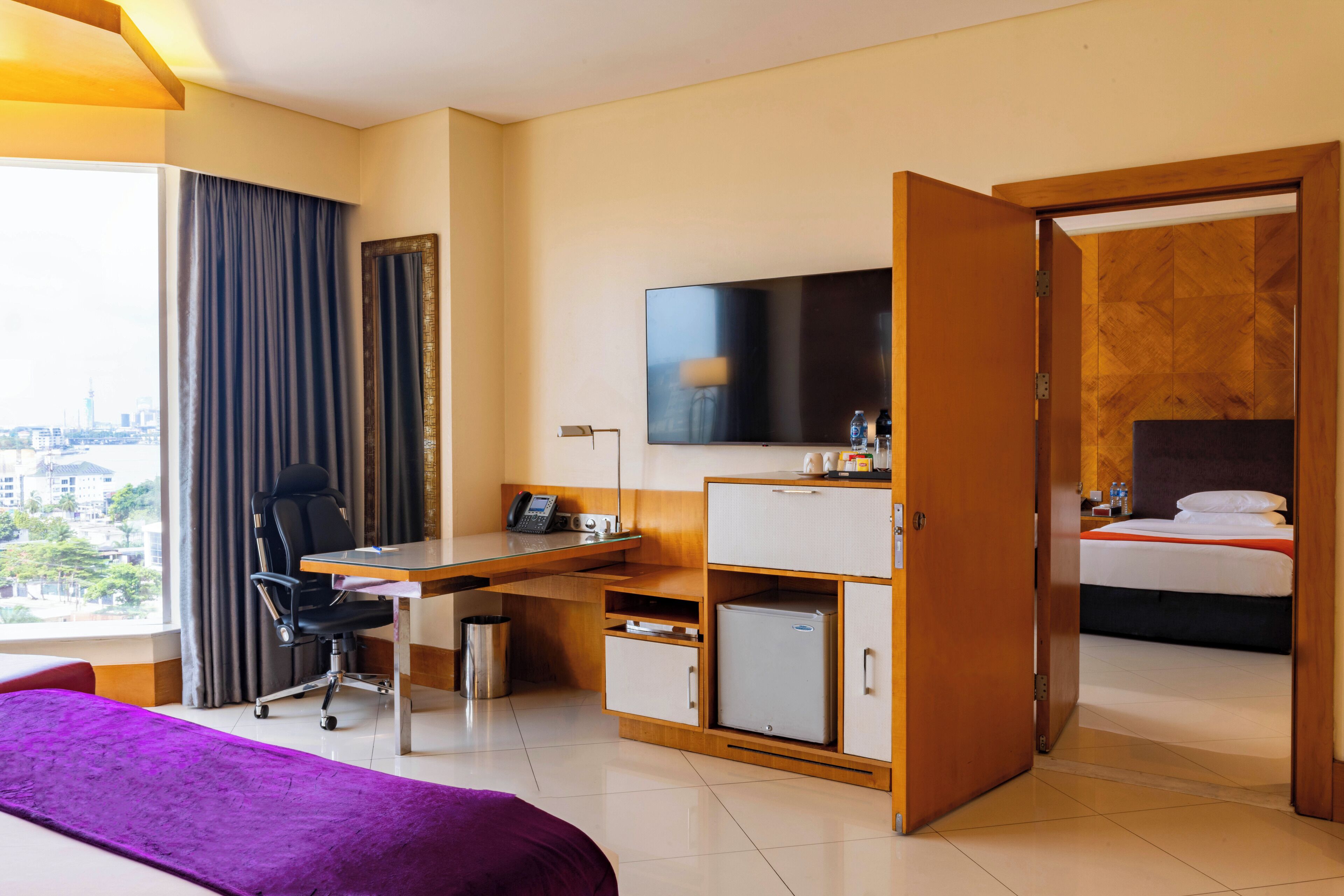 A hotel room with a bed, a desk with a chair, a television, and a wardrobe.