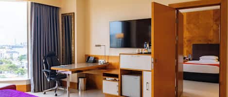 A hotel room with a bed, a desk with a chair, a television, and a wardrobe.