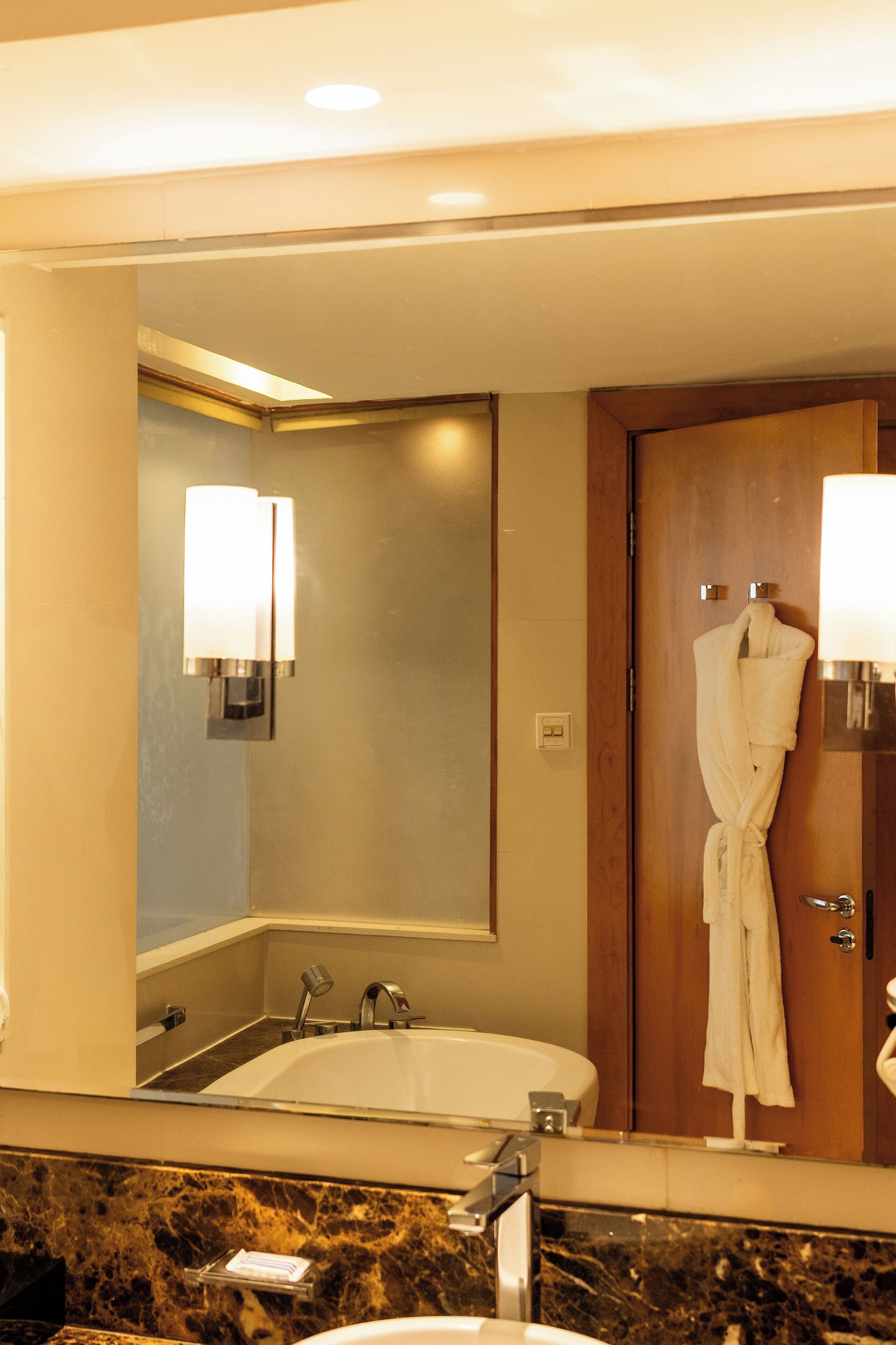 Une salle de bain d’hôtel avec un grand miroir, une baignoire, un lavabo et une robe accrochée au mur.