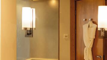 A hotel bathroom with a large mirror, a bathtub, a sink, and a robe hanging on the wall.