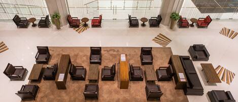 A spacious lobby with a central reception desk, multiple seating areas with chairs and tables, and large windows providing views of the outside.