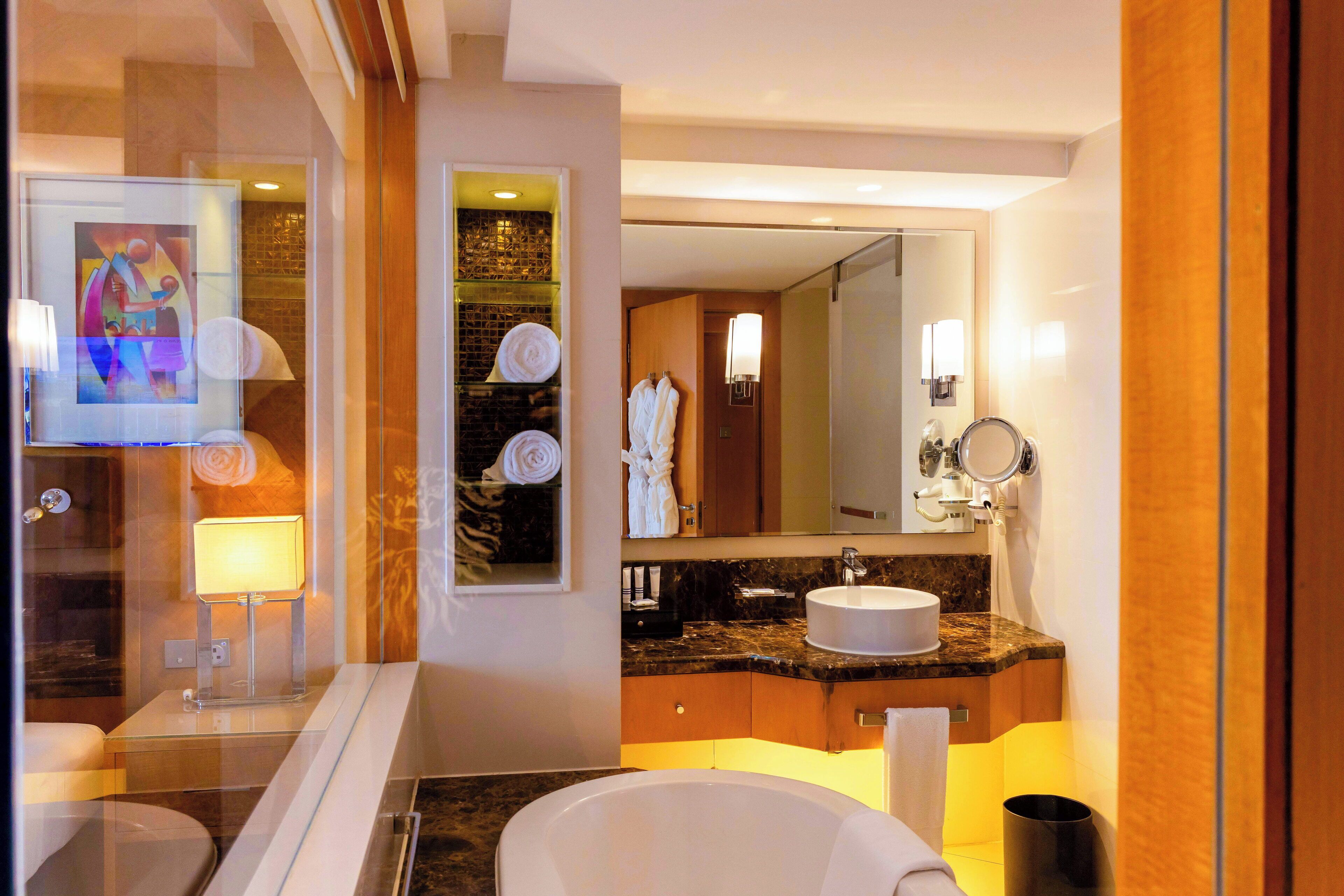 A modern bathroom with a glass partition, a marble countertop, a white sink, and a large mirror.
