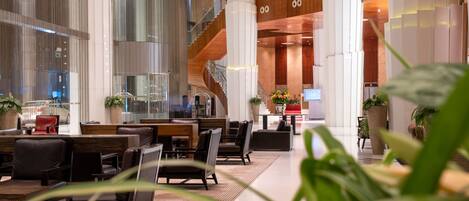 A spacious lobby with high ceilings, a central staircase, and multiple seating areas.