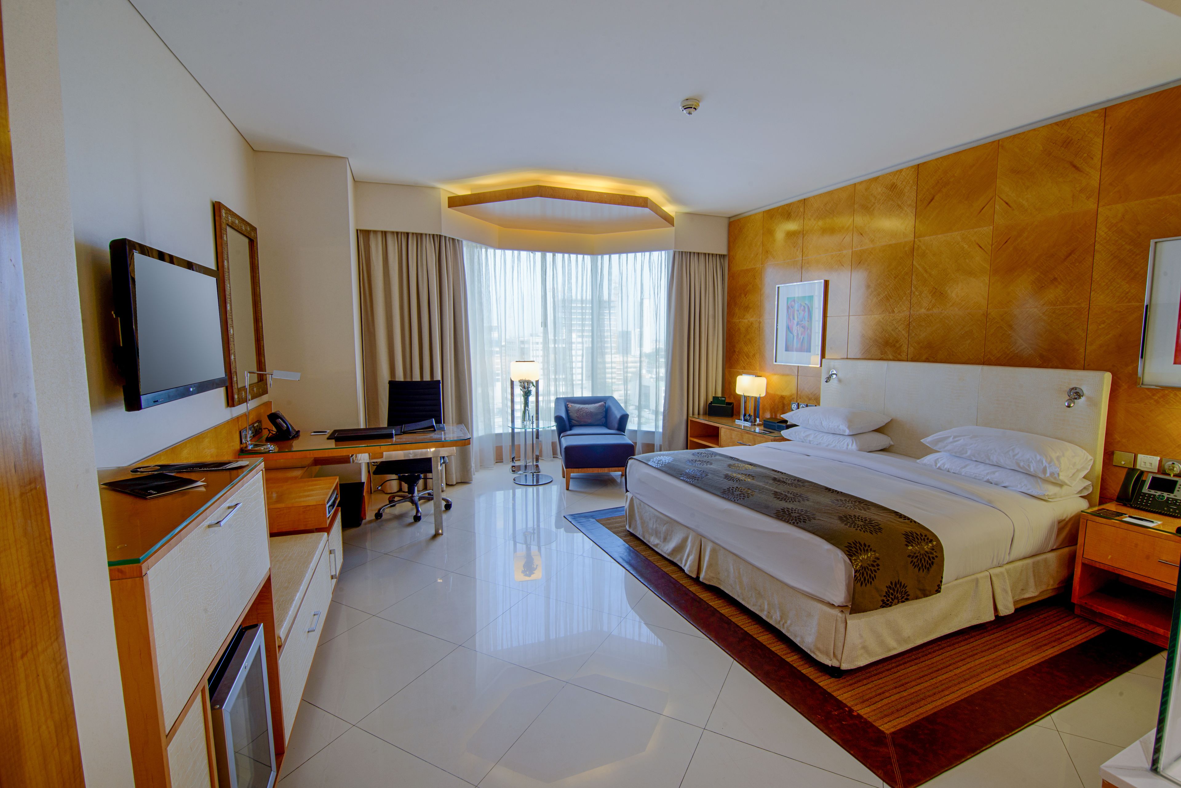 A hotel room with a large bed, a desk with a computer, a chair, and a TV.