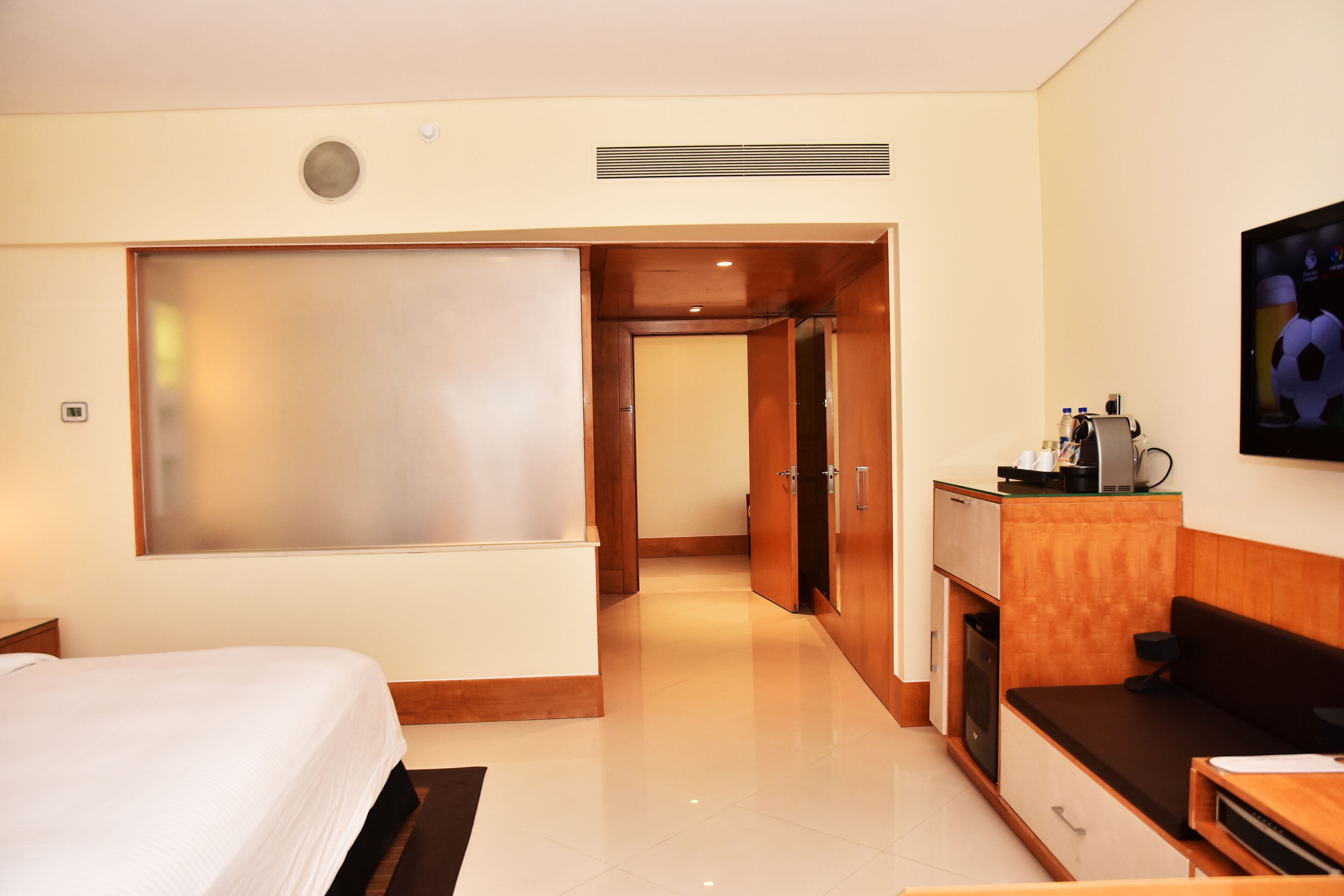 A hotel room with a bed, a desk with a computer, a TV, and a kitchenette.