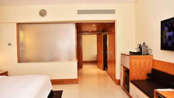 A hotel room with a bed, a desk with a computer, a TV, and a kitchenette.